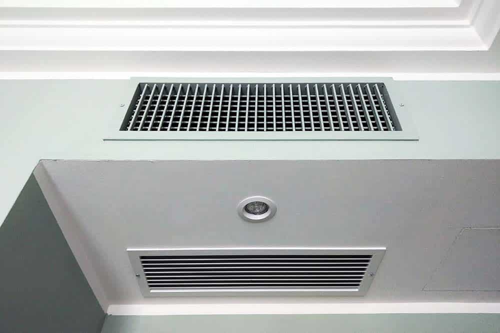 A modern, bright living room with visible air vents and a sleek, digital thermostat on the wall.
