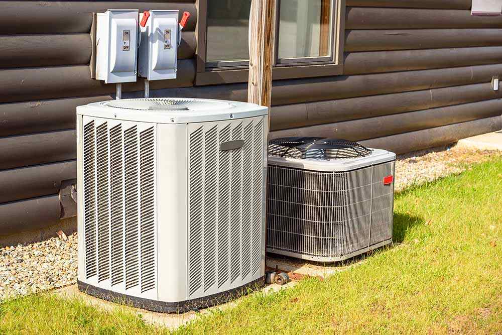 A homeowner looking at her phone, texting while standing beside an HVAC unit.