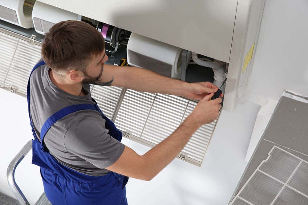 A technician repairing a central AC unit, with tools and diagnostic equipment visible.