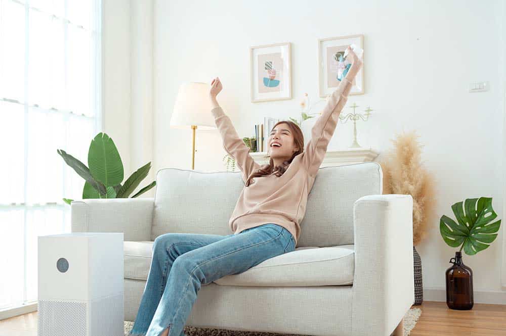 Homeowner placing air purifier beside living room sofa