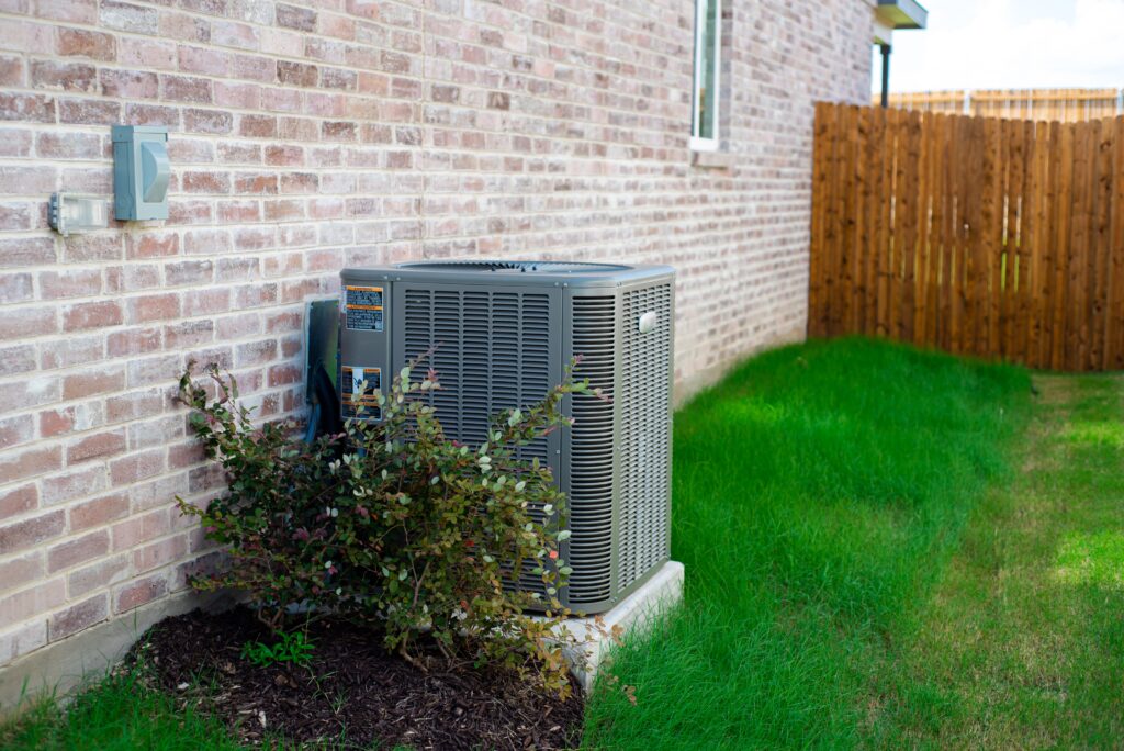 An outdoor HVAC unit beside trimmed shrubs