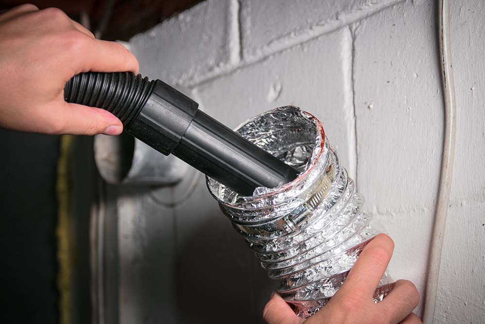 A technician cleaning air ducts with a vacuum hose