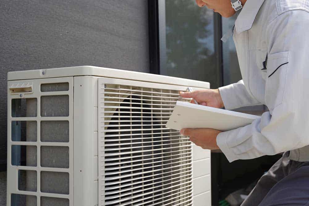 An HVAC technician checking an outdoor air conditioner unit