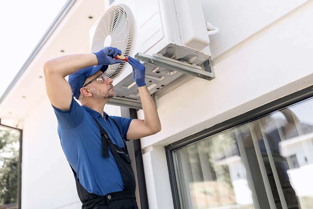 An HVAC technician repairing an air conditioning unit outdoors