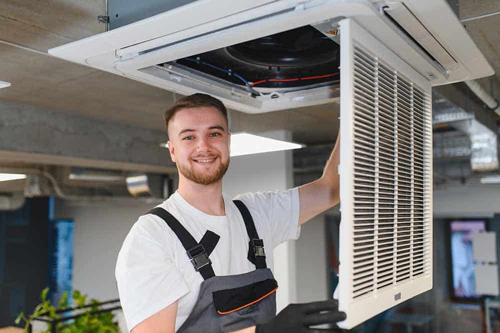 An HVAC technician brushing out a dusty air vent