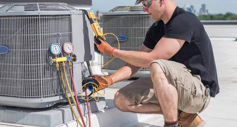 A professional HVAC technician inspecting ductwork and checking measurements on a digital tablet next to an outdoor AC unit, with sunlight in the background and tools neatly arranged nearby.