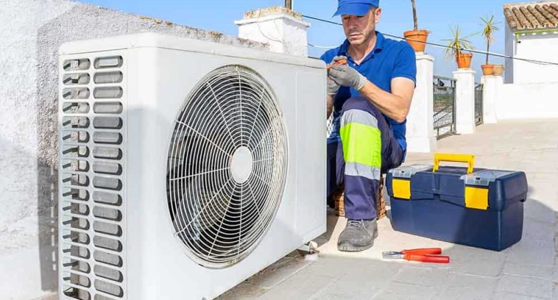 A close-up of an outdoor AC unit with a technician inspecting it, capturing a faint mist escaping from a pipe, with clear skies in the background and subtle toolkits beside the unit.