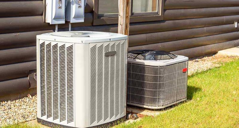 A homeowner looking at her phone, texting while standing beside an HVAC unit.
