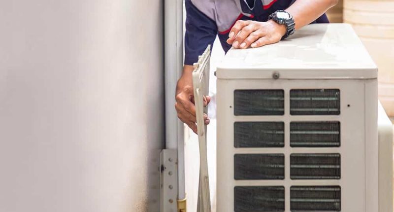 A technician inspecting a heating unit, tools in hand, with a focused, approachable demeanor. The background subtly showcases a comfortable, well-lit living room.