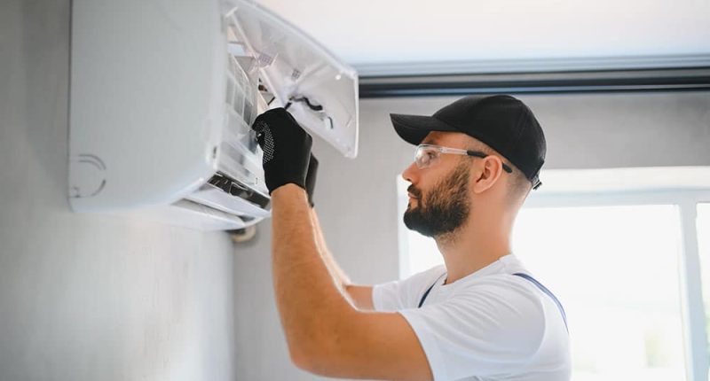 A technician servicing a modern heating unit, with tools in hand and a focused expression.